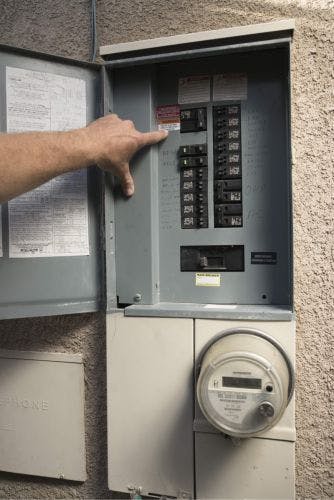 Grey electrical panel with hand pointing to the PV Breaker