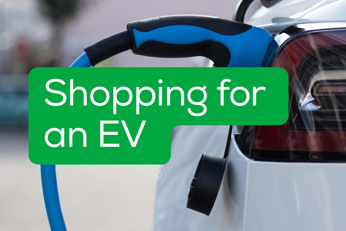 A white Tesla Model S electric vehicle is plugged into a blue EV charger, with the words, "Shopping For An EV" on a green background above it.