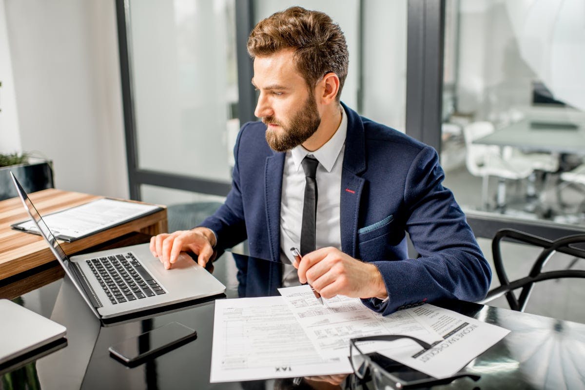 White bearded male in blue suit jacket sits at his desk, complete with financial documents, filling out Form 5695 on his laptop computer so he can claims a solar tax credit from the IRS on his federal taxes.
