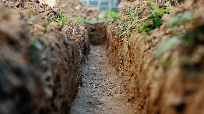 Image that shows a small trench dug through a yard to bury electrical coduit.