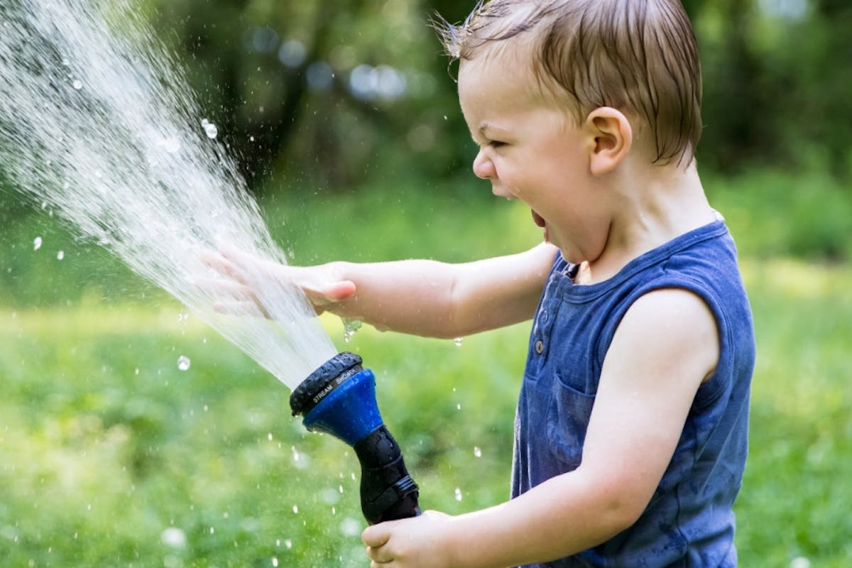 Child using a garden hose, which is an analogy to explain the electricity terms volts, amps, and watts.