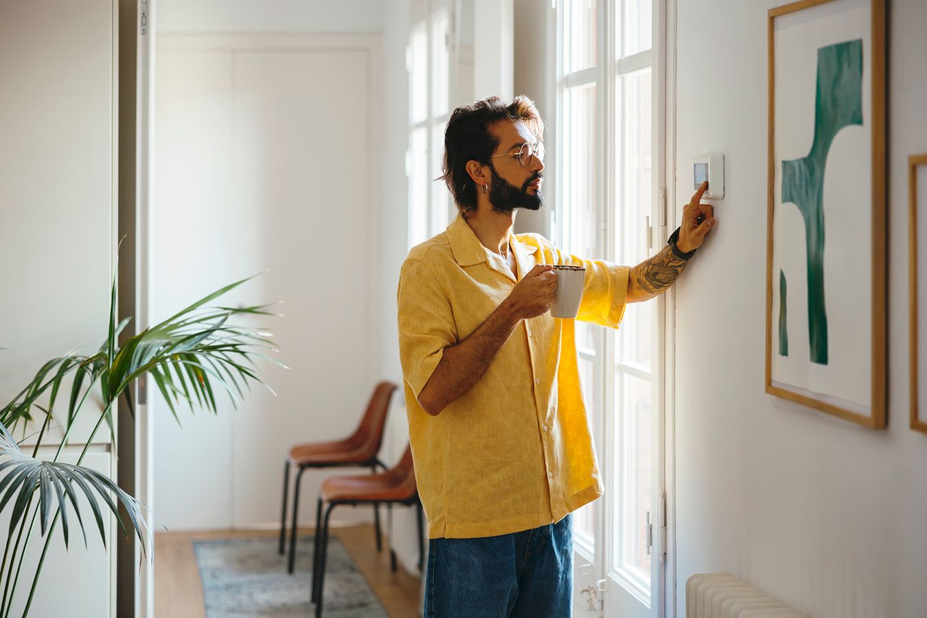A man adjusts a thermostat on the wall.
