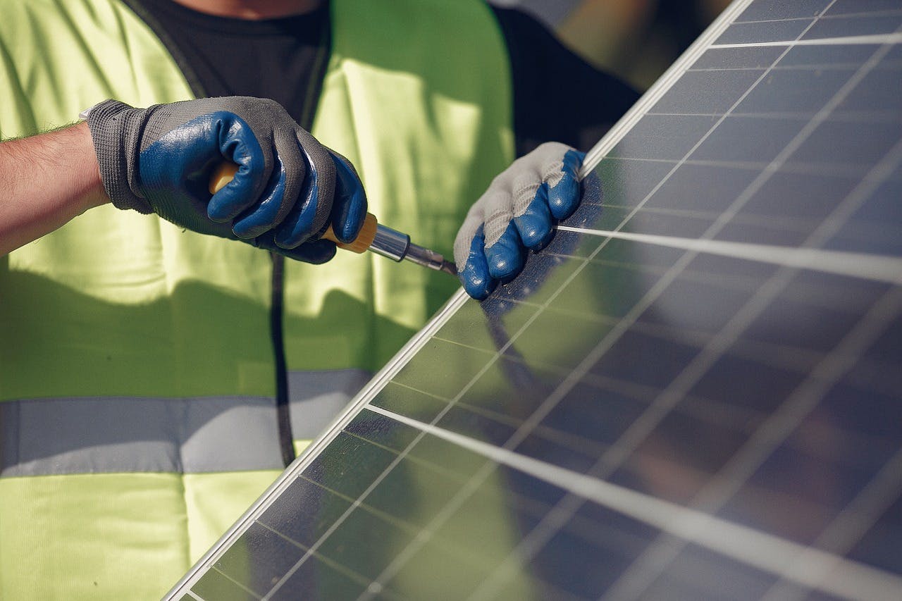 A person in a yellow vest uses a screwdriver to tighten a fastener on a solar panel.