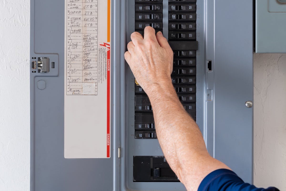 Homeowner checking a circuit breaker in their electrical panel, aka breaker box or service panel, in preparation for home solar installation.