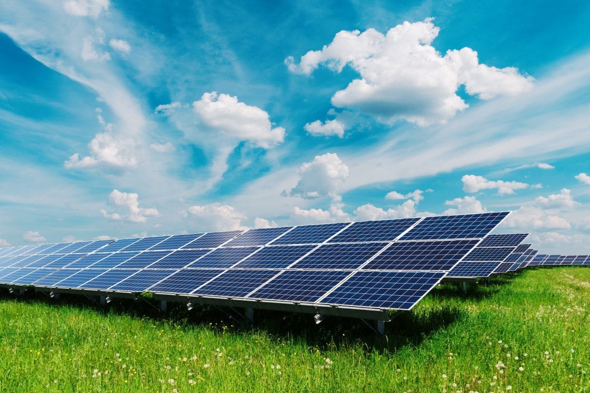 Solar panels in a field below a mostly sunny sky.