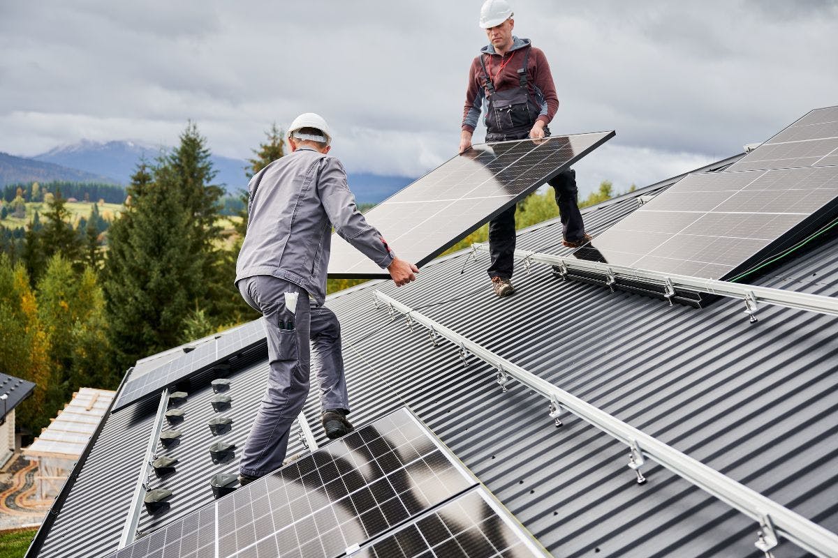 Two solar installers putting solar panels on a roof.