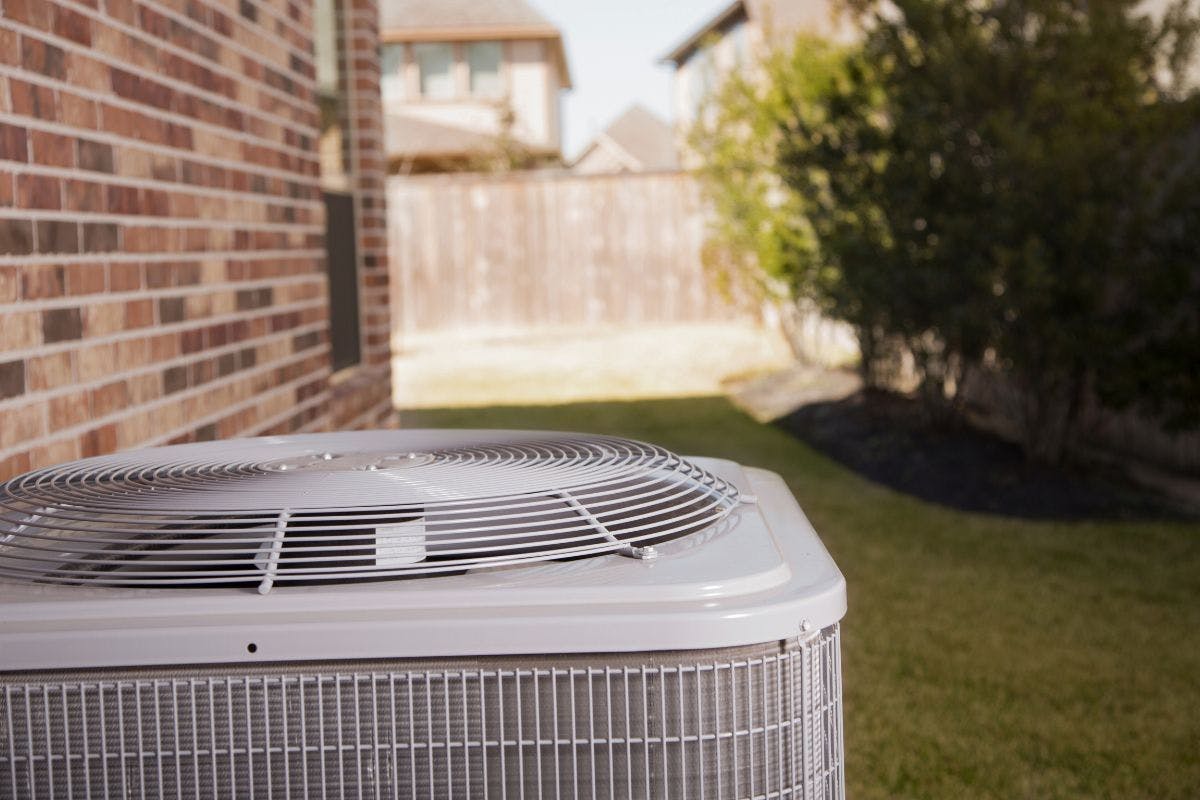 A heat pump or air conditioner exterior unit near a brick wall.