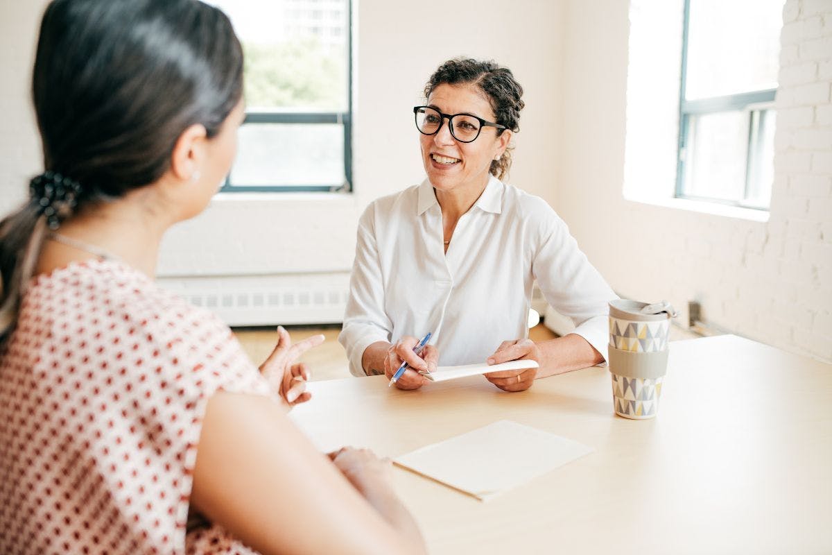 Two women at a table in a well-lit home talking.