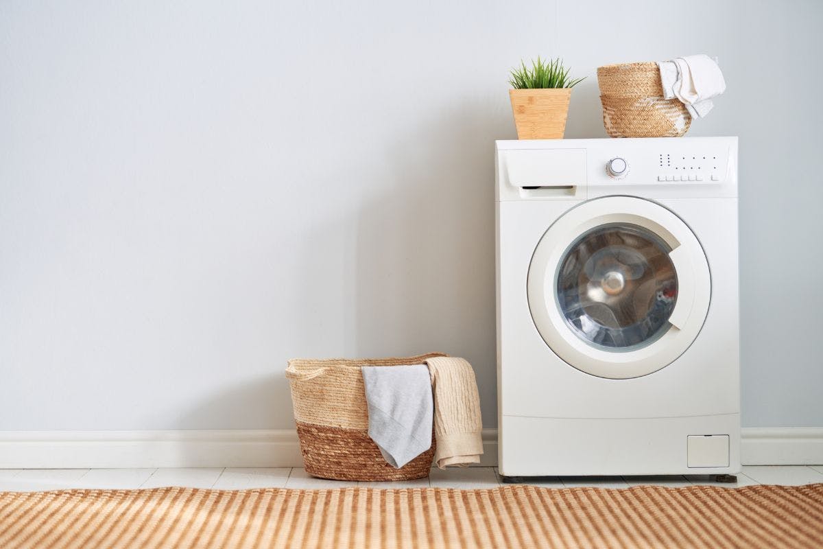 A washing machine and a laundry basket against a wall.