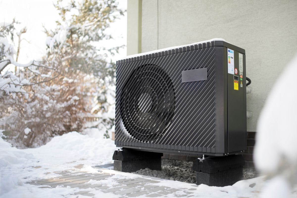 A heat pump on the exterior wall of a home with snow around.
