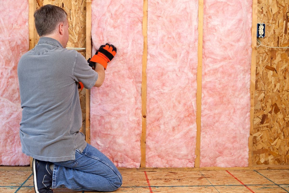 A man installing new pink insulation between the exposed studs of a wall.