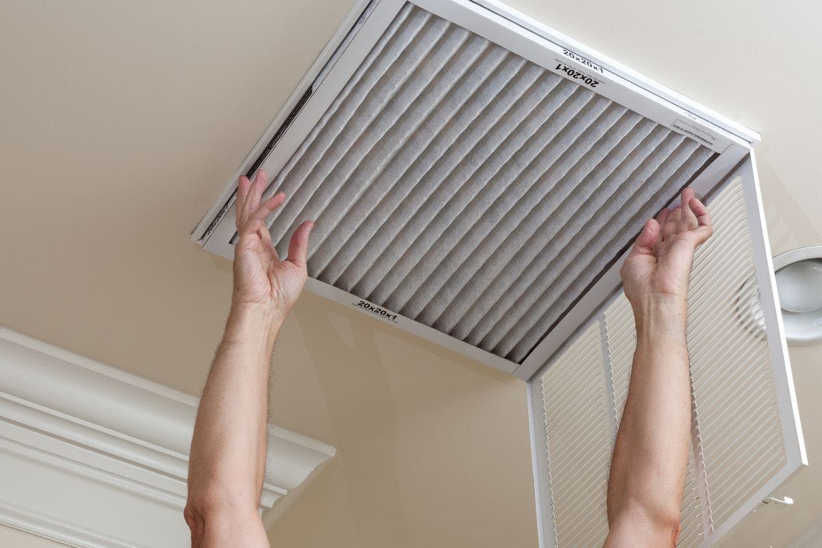 A person changes an air filter in a ceiling air intake.