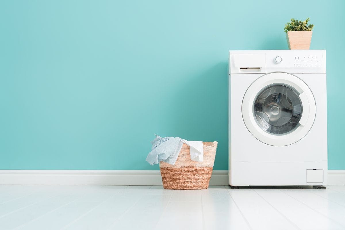 A laundry machine and a basket of laundry against a blue wall.