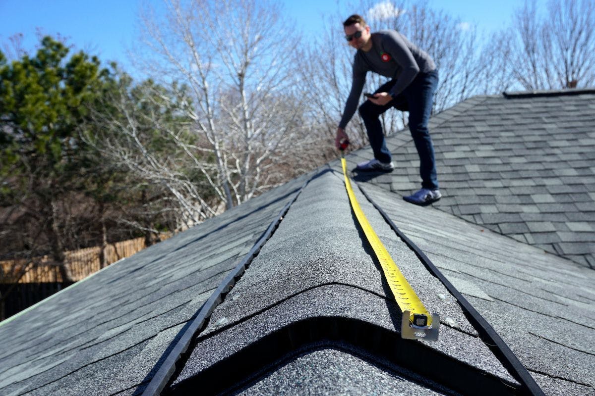 A man measuring the peak of a roof with a yellow measuring tape.