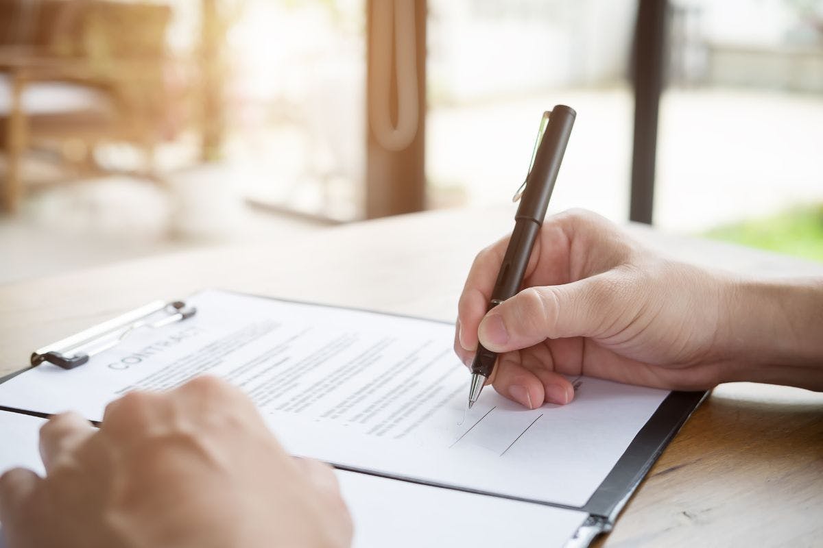 A person signing a document near some brightly lit windows.
