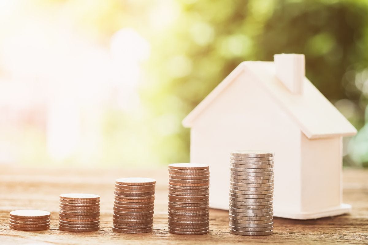 A model of a home with stacks of coins increasing in size in front of it.