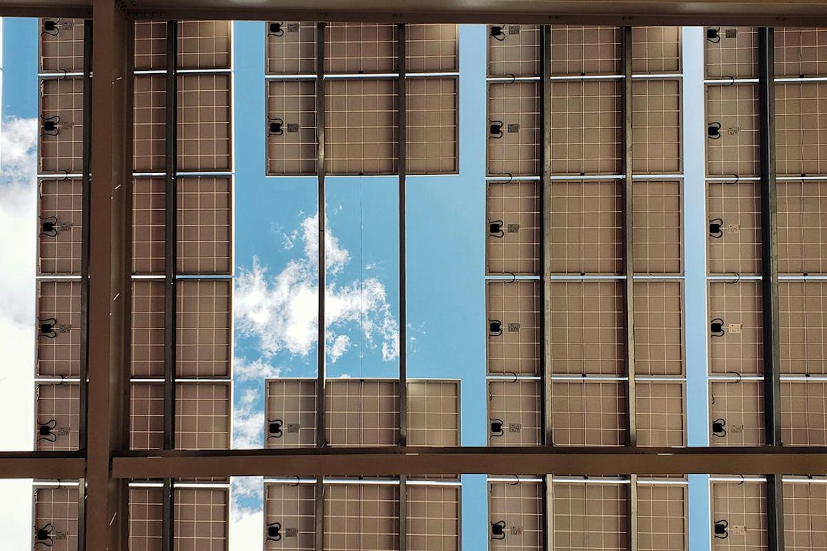 Solar panels viewed from below with a blue sky with white clouds above.