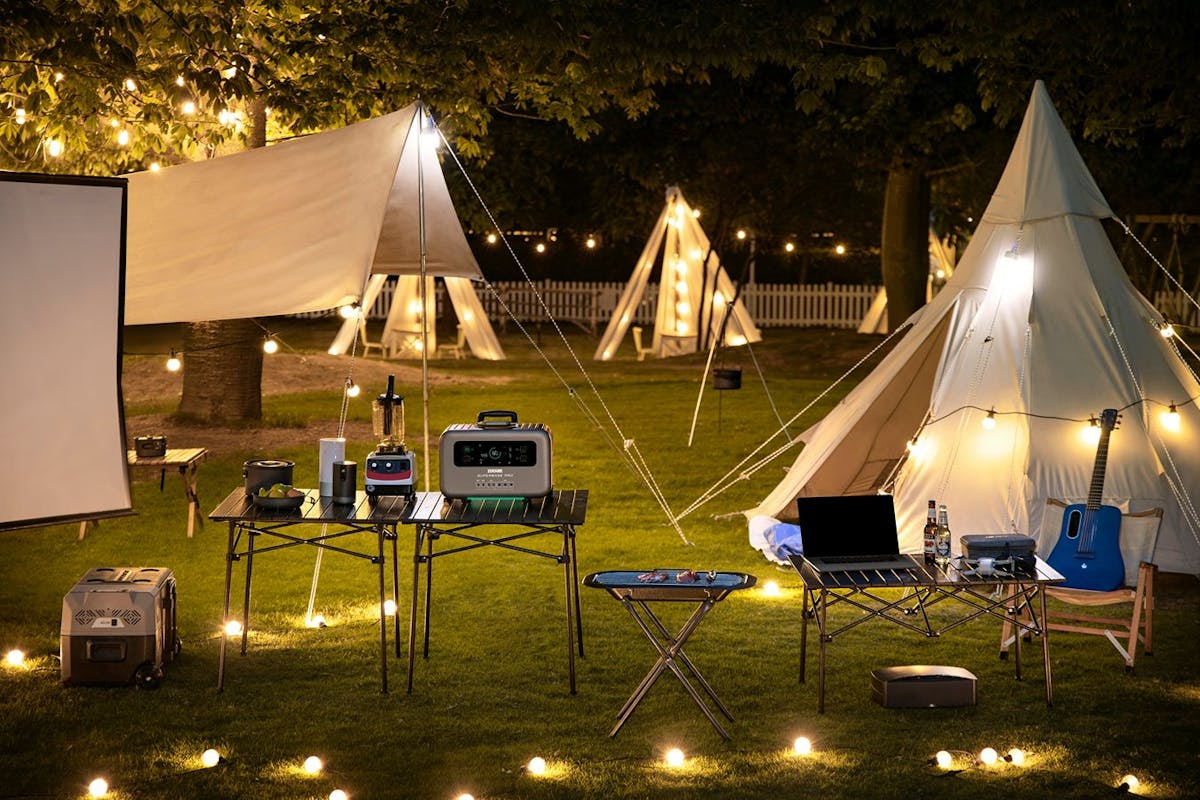 A portable power station sitting outside surrounded by electronic devices, string lights, and electric lanterns.