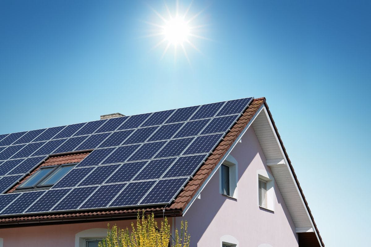 Solar panels cover a large tile roof on a white house.