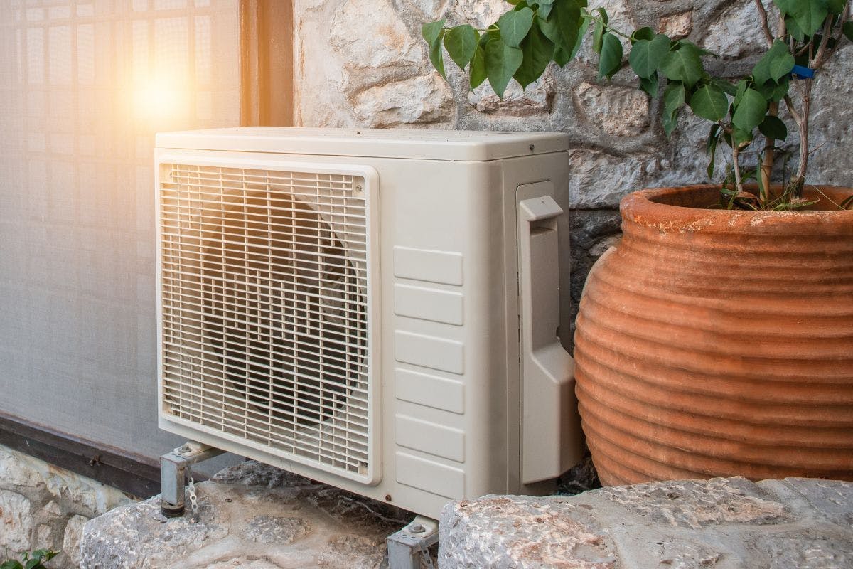 A heat pump sitting against an exterior wall near a potted plant.
