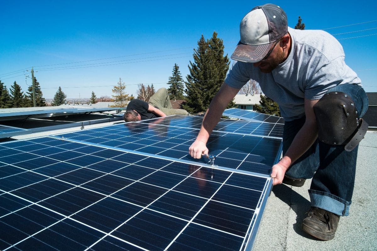 Two solar technicians work on rooftop solar panels.