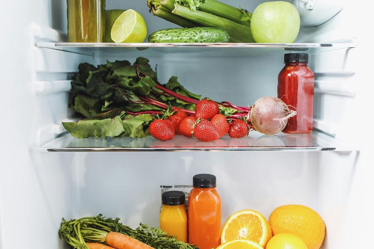 The interior of a refrigerator with colorful fruits, vegetables, and juice.