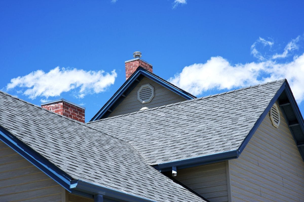A house's shingle roof beneath a blue sky.