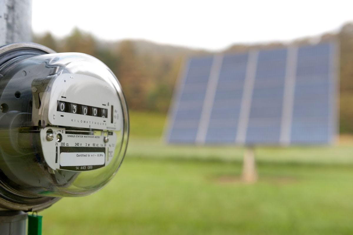 An electric meter with solar panels in the background.