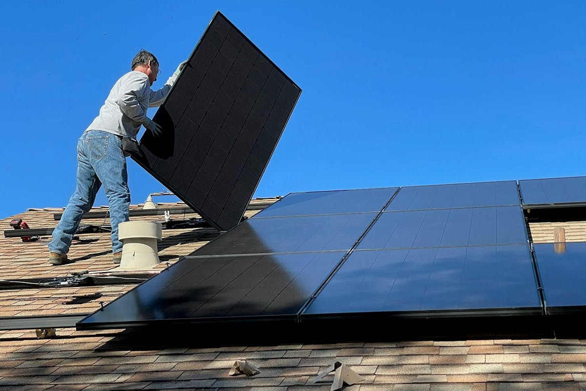 A man installing solar panels on a shingle roof.