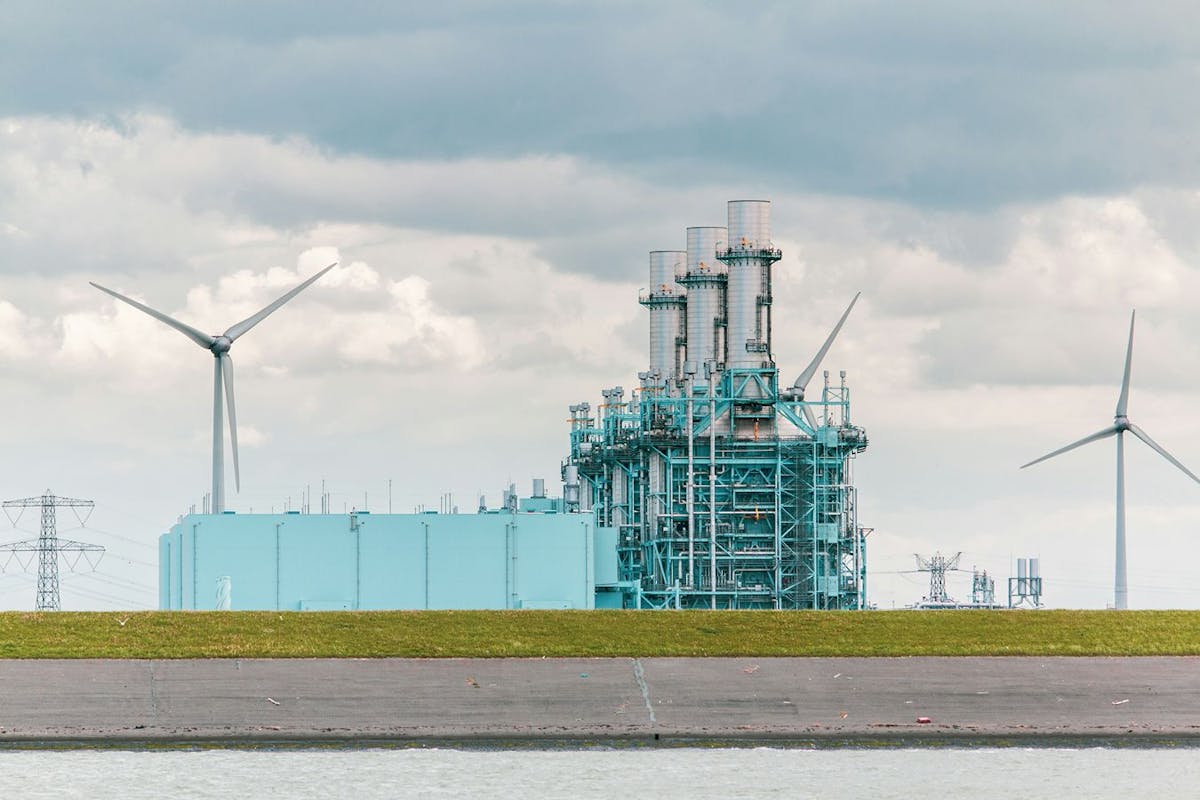 Wind turbines and power lines near an industrial-looking building.