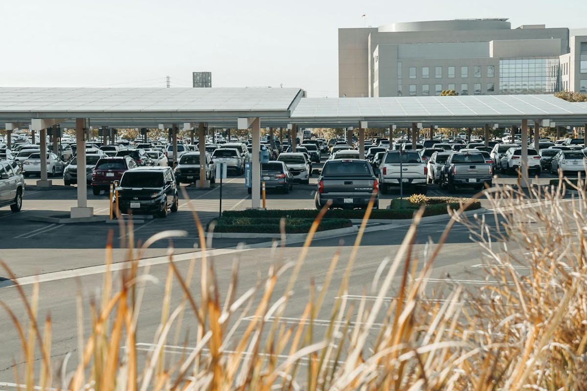 A parking lot with solar canopies in front of a large building in the sun.