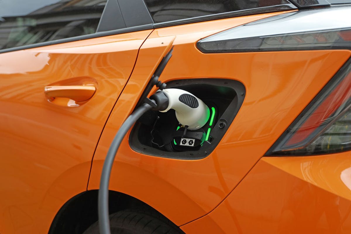 An EV charger plugged in to an orange EV.