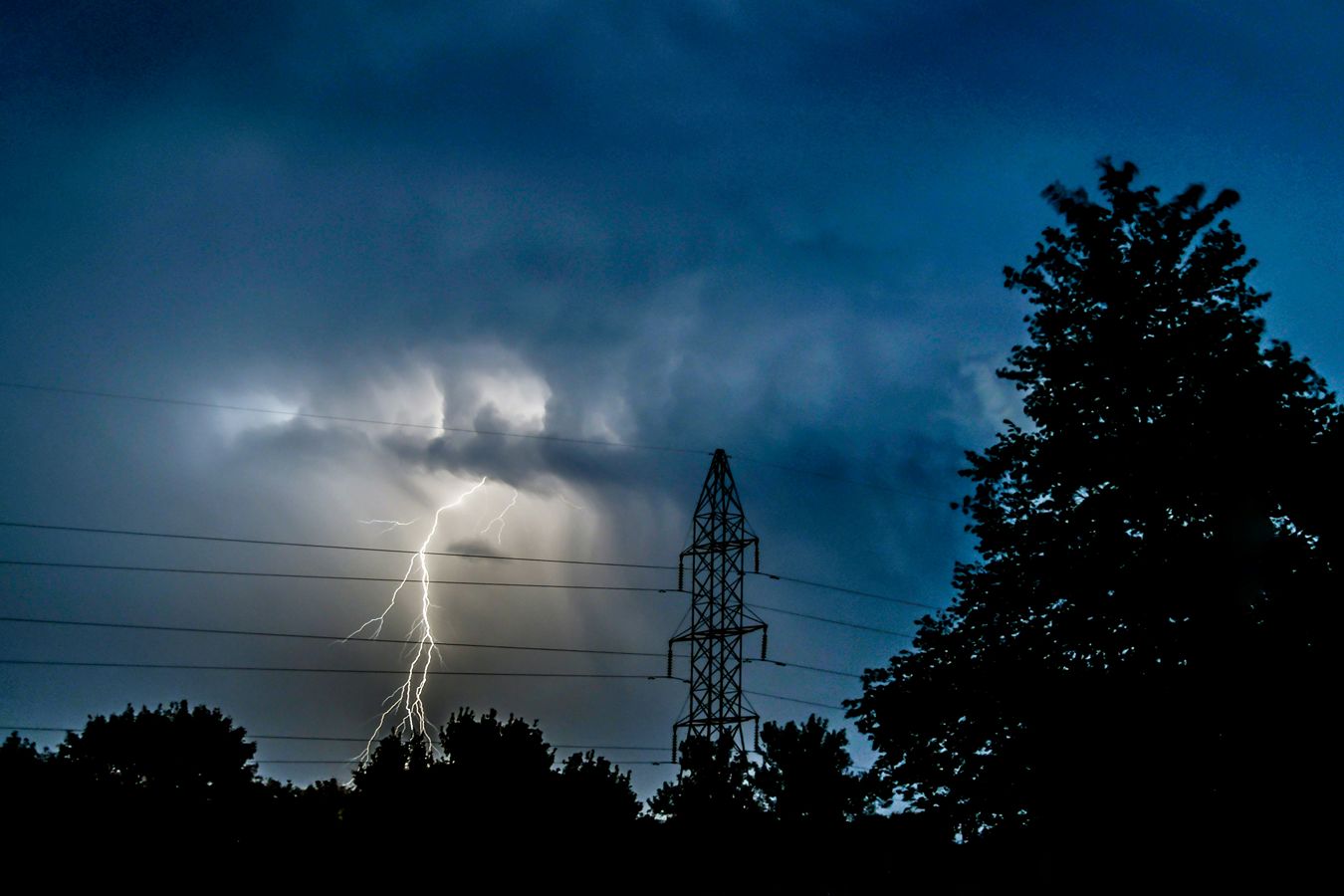 Lightning strikes behind power lines on a stormy night.