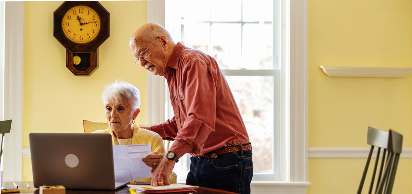 Two senior citizens viewing a paper bill and a laptop.