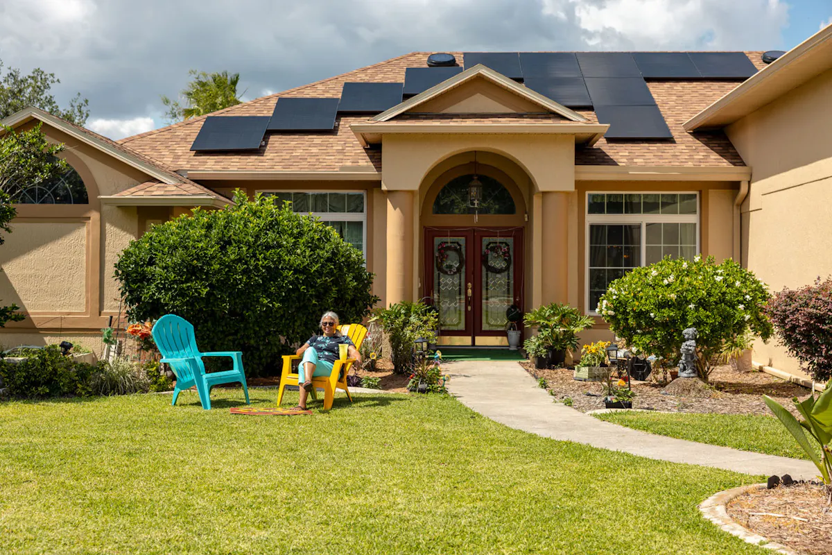 Geraldine sitting outside her home with solar panels on the roof.