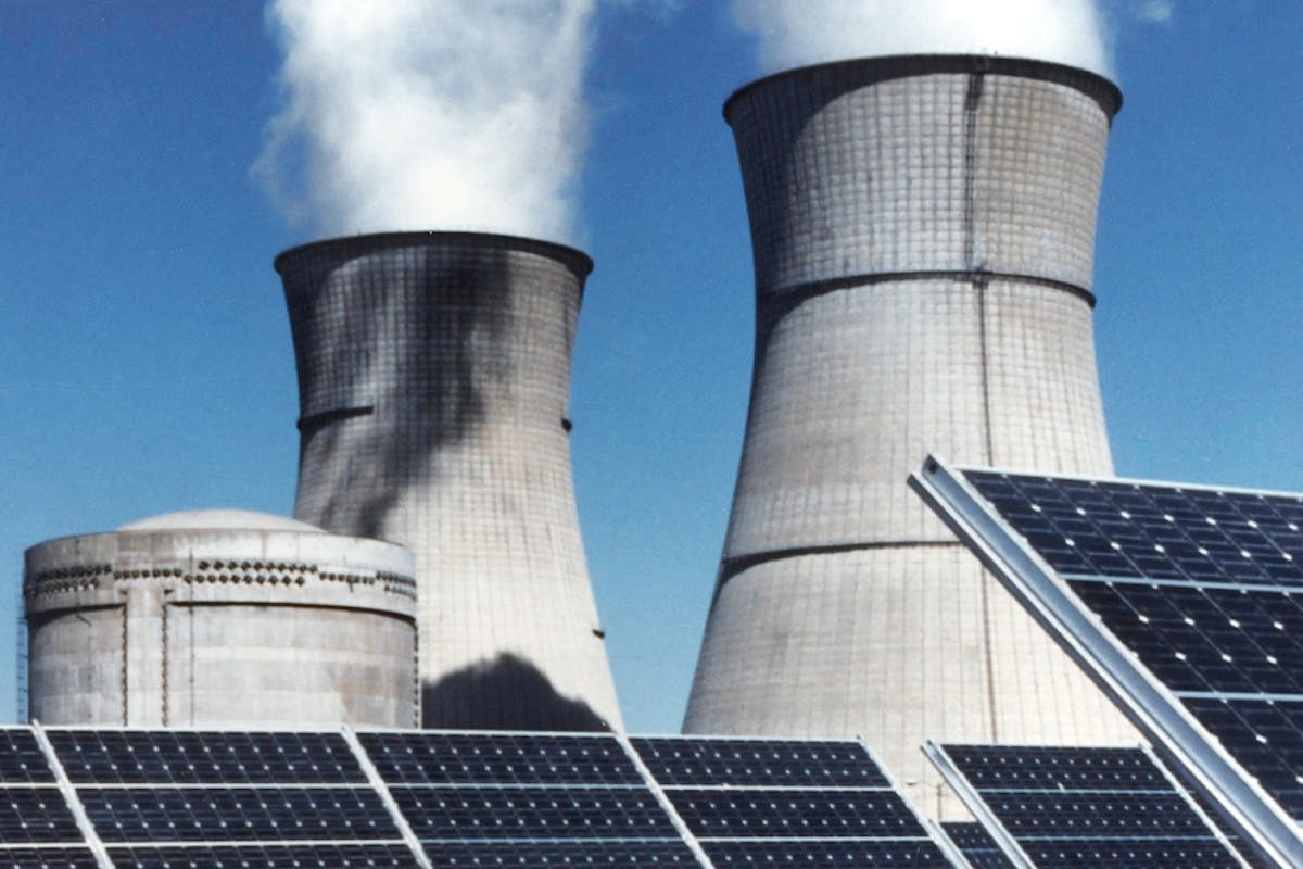 Solar panels in front of a fossil fuel power plant, highlighting the benefits of clean energy.