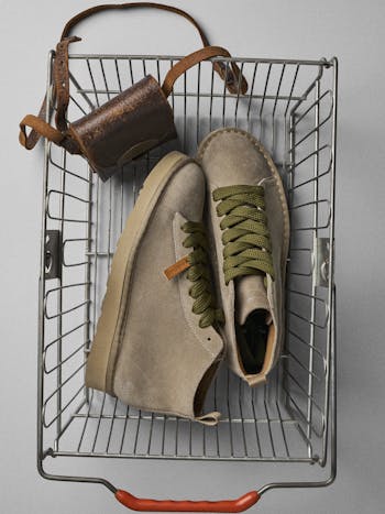 A pair of P001 ankle boots are placed in a shopping basket alongside a small leather pouch.