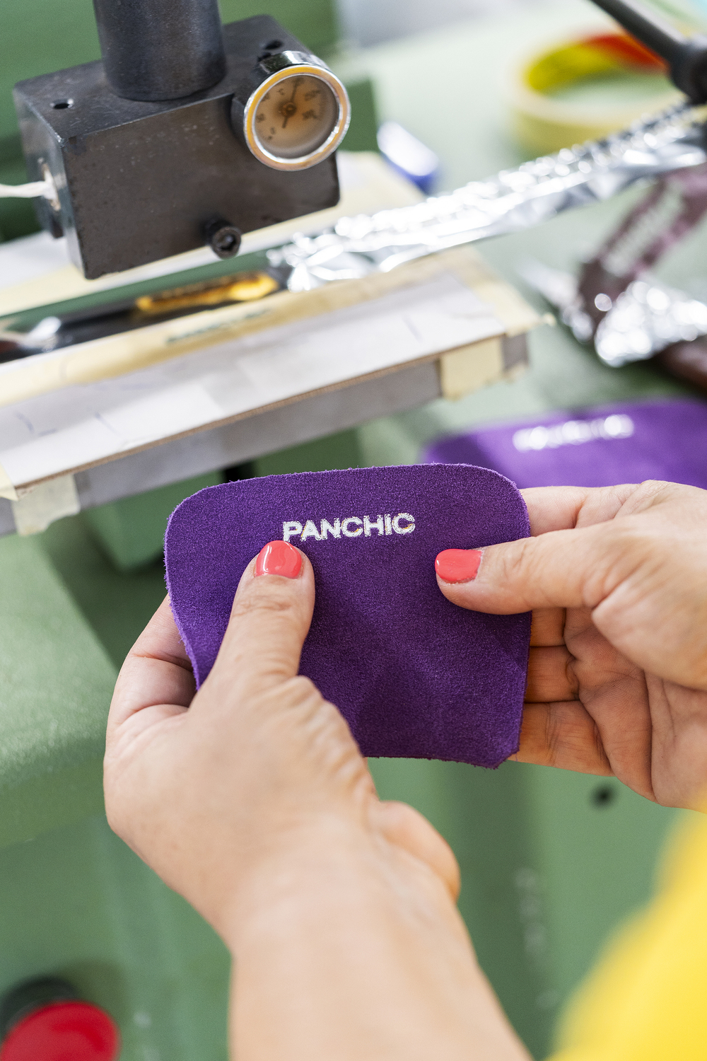 Two hands hold a purple shoe tongue with the print of PANCHIC's logo