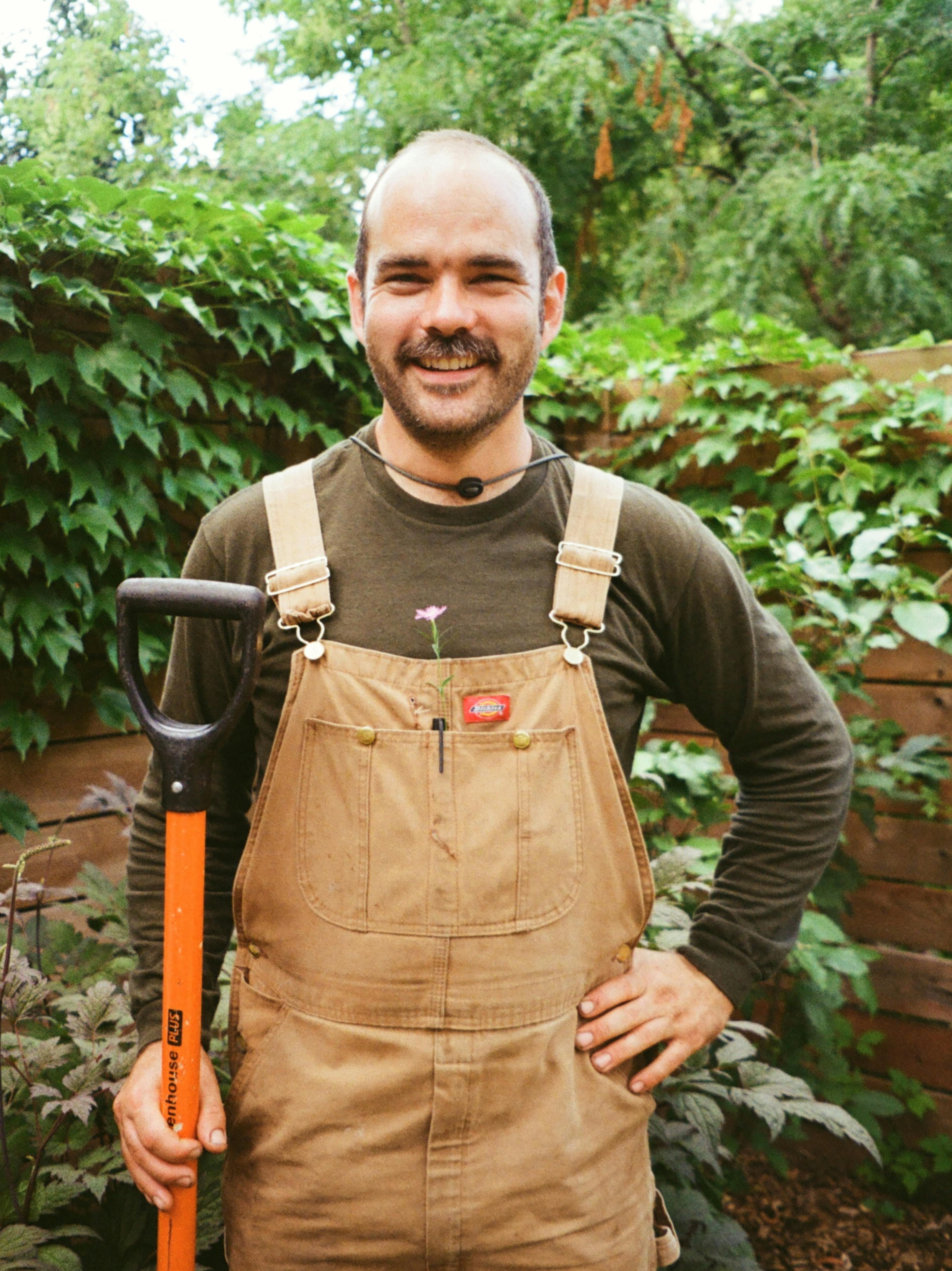 Directeur général de l’entreprise d’aménagement paysager écologique Pansy, debout dans un jardin avec salopette et pelle, représentant le design durable à Montréal.
