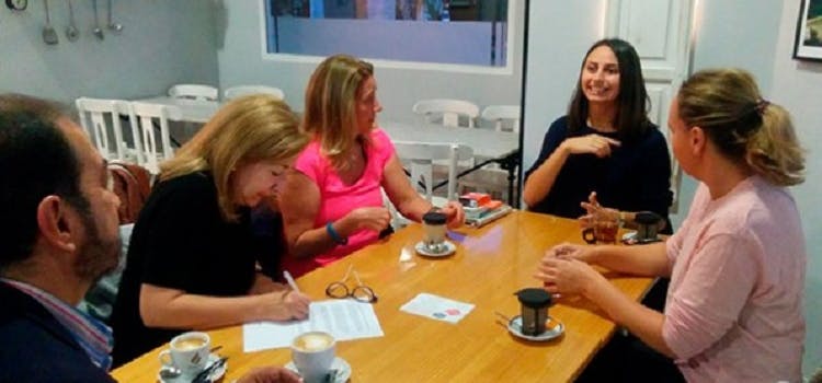 Personas sendadas en una mesa escribiendo y tomando café | My English Moment en escuela de inglés