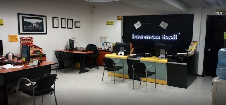 Recepci&oacute;n de una de las sedes de Harmon Hall en M&eacute;xico | Paredes blancas y negras, con un cartel luminoso del nombre de la escuela, muchas sillas y escritorios.