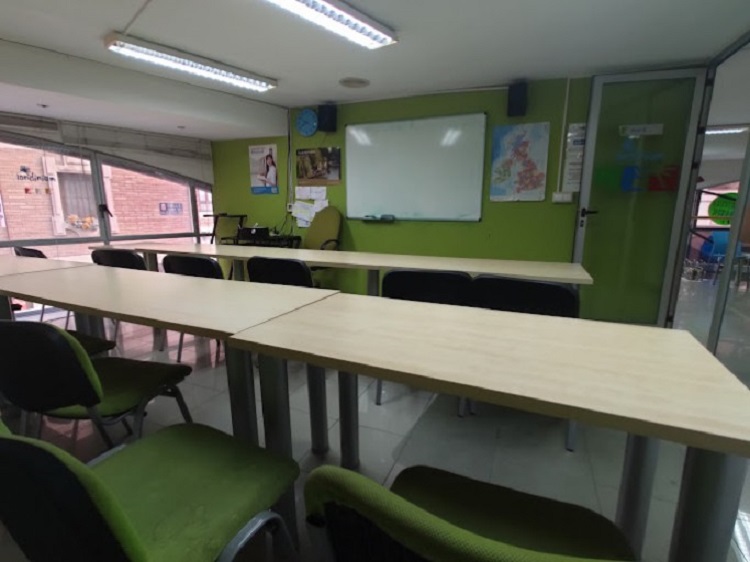 Sal&oacute;n de clases de color verde con una pizarra, muchos mesones y sillas | Londinium Idiomas