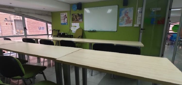 Salón de clases de color verde con una pizarra, muchos mesones y sillas | Londinium Idiomas
