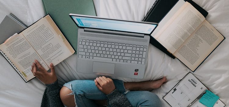 pc sobre la cama y libros de estudio