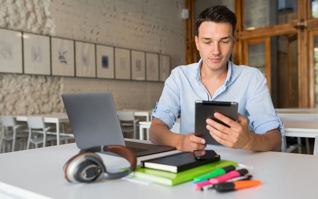 Junge Mann, der mit PC und Handy an einem Tisch lernt