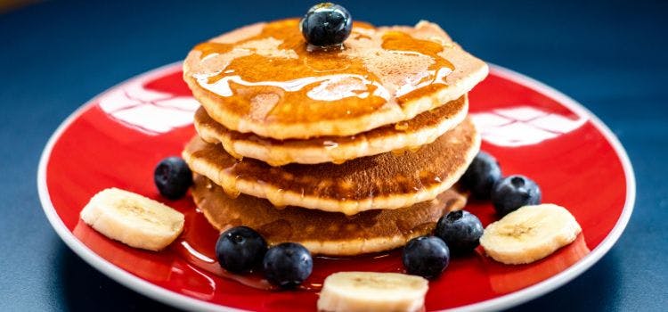 fotografía de un pancake con arándanos en plato rojo