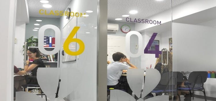 Salones de clases de Shamrock idiomas | Cubiculos con paredes de vidrio, mesas, sillas y personas viendo clases.