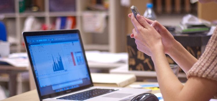 Persona con una laptop al frente sonteniendo un móvil