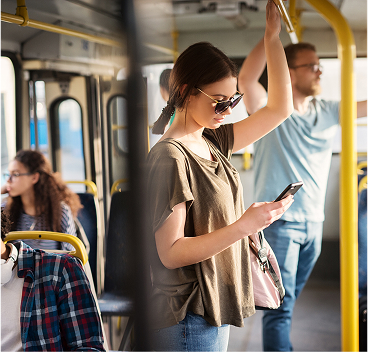 Passengers riding a public transit bus, with one person standing and using a smartphone, suggesting access to onboard Wi-Fi or mobile connectivity.