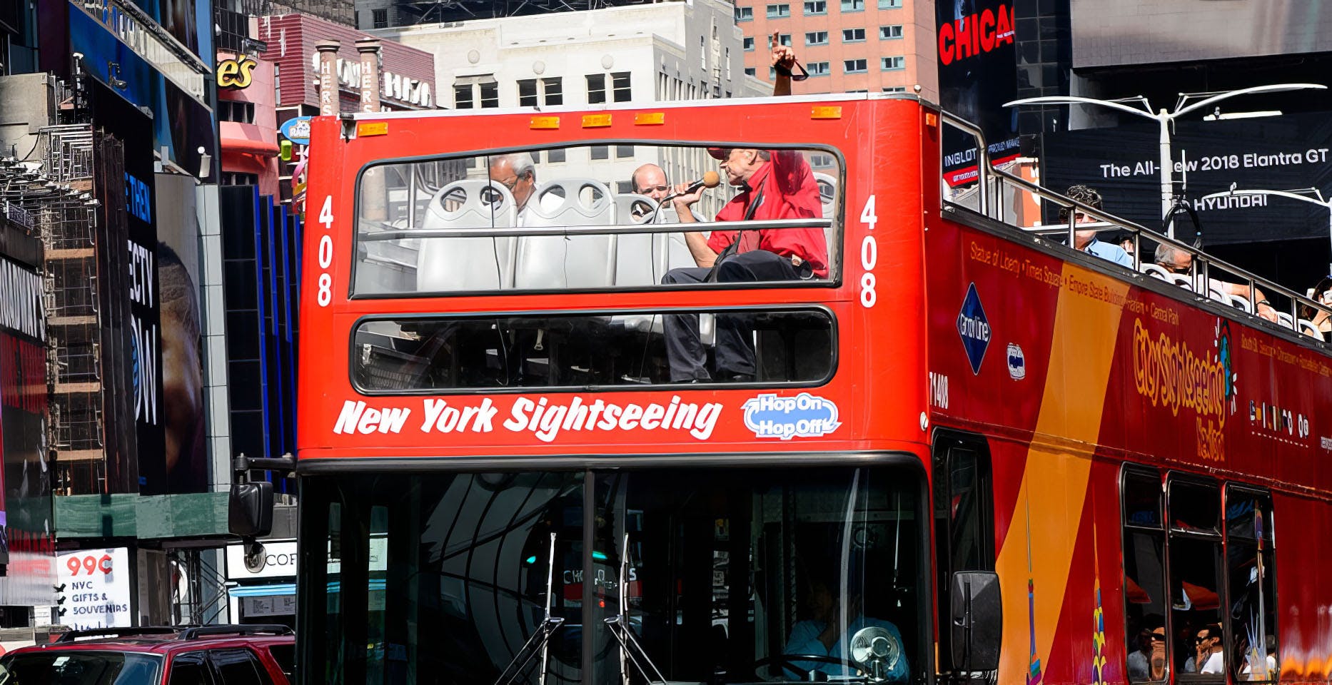 Red double-decker New York sightseeing bus with passengers seated on the upper deck and a tour guide speaking into a microphone, representing real-time transit experiences enhanced by Passio GO™.
